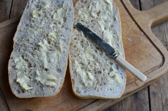 Method: 1. Cut the loaf of bread in half as seen in the photos. 2. Spread both halves of the bread with the butter and then layer up the ingredients on one half of the bread loaf in the order listed – see the photos. 3. Place the lid on top of the filling and then wrap in greaseproof paper and tie with some string. 4. Place some heavy books or weights on top and leave for at least 12 to 24 hours, in a cool place. 5. Serve in slices.