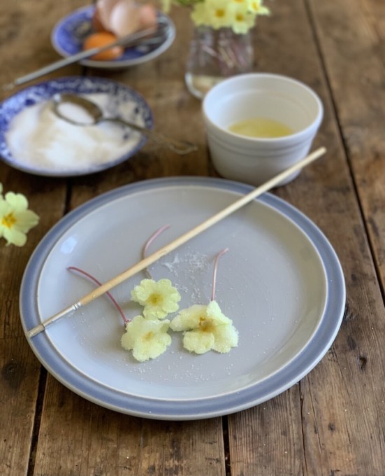  Place the dry fresh primroses on a breadboard, baking tray or flat surface. Beat the egg white to a light foam. Brush the flowers all over with beaten egg white, using a soft pastry brush or a paint brush.