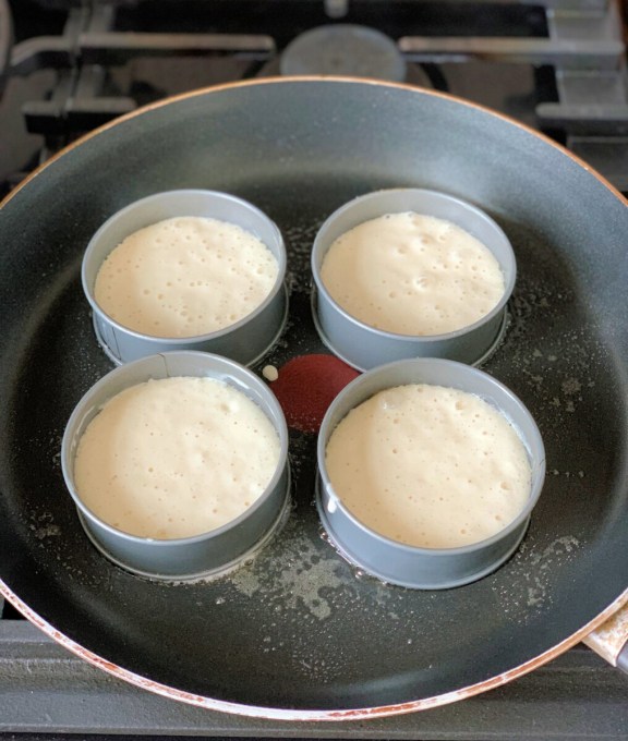 Brush inside each crumpet ring with melted butter or spray with the oil. Heat the frying pan over a low heat and then grease the pan with butter or spray oil. Place the greased crumpet rings in the frying pan.